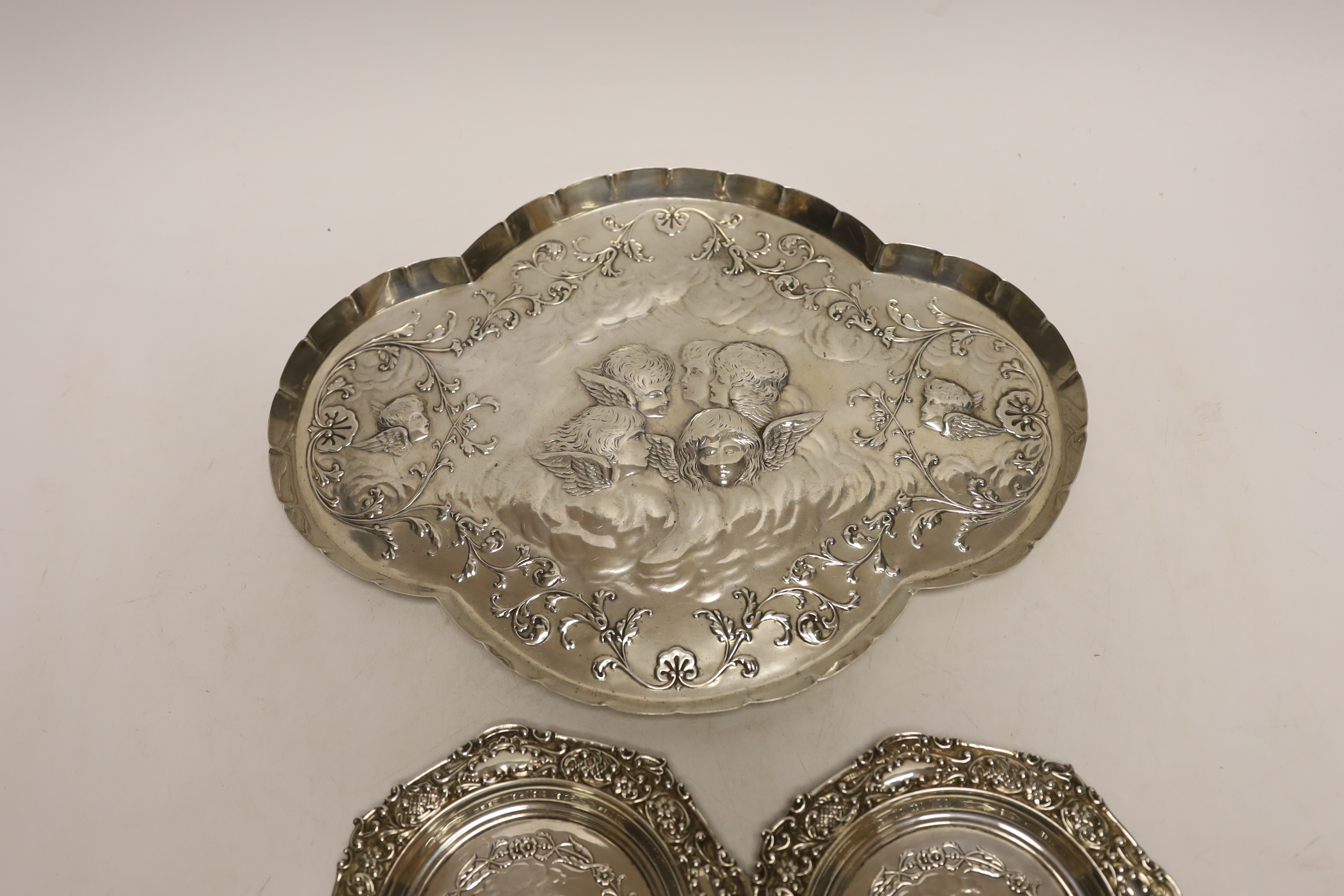 A late Victorian repousse silver dressing table tray with Reynold's Angels decoration, William Comyns, London, 1899, 30.9cm and a pair of smaller similar dishes by Henry Matthews, Birmingham, 1899, 14.2oz.